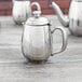A Vollrath stainless steel creamer with a lid on a table.