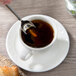 A Villeroy & Boch white porcelain saucer with a cup of coffee and a spoon on a table.