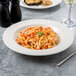 A Villeroy & Boch white porcelain rim soup bowl filled with pasta and a glass of wine on a table.