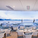 A white Bromic Platinum Smart-Heat outdoor patio heater above a table and chairs on a deck overlooking a body of water.