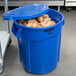 A blue Rubbermaid BRUTE trash can filled with potatoes.