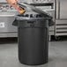 A person putting a lemon in a black Rubbermaid trash can.