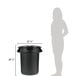 A woman standing next to a black Rubbermaid BRUTE trash can with a black lid.