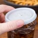 A hand holding a Cambro translucent plastic lid over a glass of liquid.