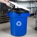A person putting a white lid on a blue Rubbermaid recycling can.