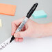 A hand using a Sharpie to write on a blue post-it note.