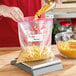 A person pouring macaroni into a Ziploc plastic bag.