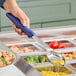 A hand holding a blue Vollrath Jacob's Pride Spoodle over a bowl of food.