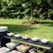A Vollrath black wood long narrow shelf holding a row of white bowls of food on a table.