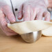 A person in gloves holding a stainless steel hemisphere mold filled with dough.