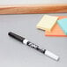 A black Expo dry erase marker on a table next to a yellow sticky note.