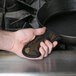 A hand holding a Lodge camouflage handle holder over a pan.