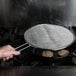 A hand using a Lodge splatter screen over a pan with food cooking.