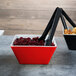 Two red and black Vollrath melamine bowls with cranberries on a table.