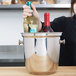 A woman holding a bottle of wine in a Vollrath stainless steel wine bucket on a table.