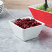 A white small square melamine bowl filled with cranberries with a spoon