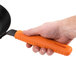 A hand using an orange Lodge handle holder on a black skillet.