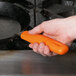 A hand holding an orange Lodge silicone handle holder on a pan.