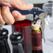 A hand with a blue Pullparrot Waiter's Corkscrew opening a wine bottle.