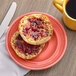 A Tuxton Concentrix Cinnebar china plate with a muffin and jam on it, with a cup of coffee.