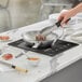 A person using an Avantco countertop induction cooker to cook meat in a pan.