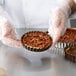 A person wearing plastic gloves holds a small fluted tart.