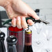 A person using a Pulltap's Original dark green Waiter's Corkscrew to open a bottle of wine.