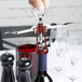 A hand using a Franmara Tavern Wing Corkscrew with a red and silver body to open a bottle of wine.