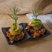 Two black matte melamine sauce dishes with food on them and a sprig of rosemary.