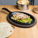 A Lodge oval cast iron fajita skillet with food on a table.