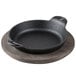 A Lodge mini cast iron casserole dish with walnut wood underliner on a table.