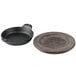A Lodge mini cast iron round casserole dish with walnut wood underliner on a round wooden plate.
