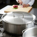 A woman using a Vollrath stainless steel cover to prepare food in a large pot.