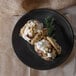 A Nara black melamine plate with two cookies and cream on it.