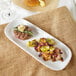 A rectangular melamine platter with a plate of food including meat and vegetables on a table.