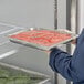 A person holding a Vollrath stainless steel tray of food.