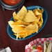 A blue HS Inc. oval basket filled with blueberries on a table with a plate of chips and salsa.