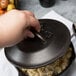 A person using a Lodge Pre-Seasoned Cast Iron Dutch Oven lid.