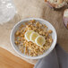 An ivory melamine oval bowl filled with cereal and sliced bananas with a glass of milk on the side.