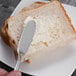 A Oneida Scroll stainless steel butter knife cutting a piece of bread with butter.