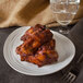 An oval ivory melamine platter with a textured rim holding chicken wings and a glass of water.