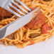 A Oneida Scroll stainless steel dinner knife and fork cutting into spaghetti with sauce.