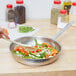 A person stirring vegetables in a Vollrath stainless steel fry pan.