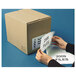 A person holding a box of Quality Park white business envelopes next to papers.