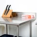 An Advance Tabco stainless steel work table with knives and a cutting board on it.