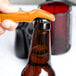 A hand using a yellow Franmara plastic bottle opener to open a brown bottle.