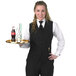 A woman wearing a Henry Segal black server vest holding a tray.