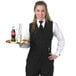 A woman in a Henry Segal black server vest holding a tray.