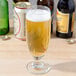 A Libbey stemmed pilsner glass of beer on a table next to other bottles.