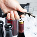 A hand holding a Franmara black two-lever corkscrew over a wine bottle.